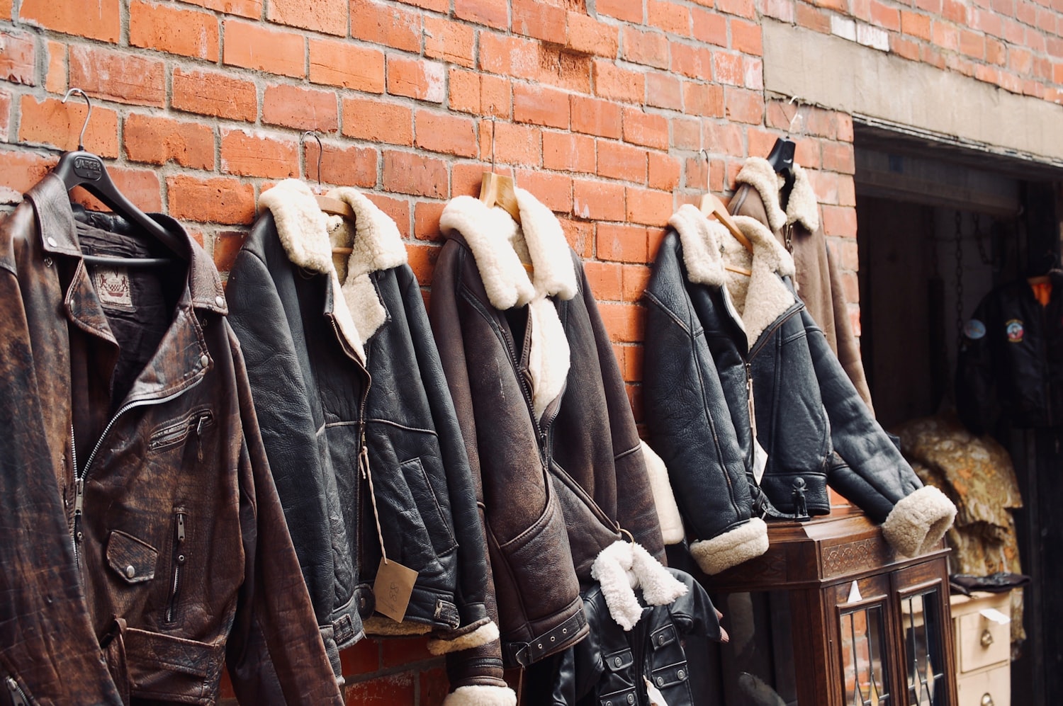 Vintage leather and shearling jackets hanging on a brick wall.